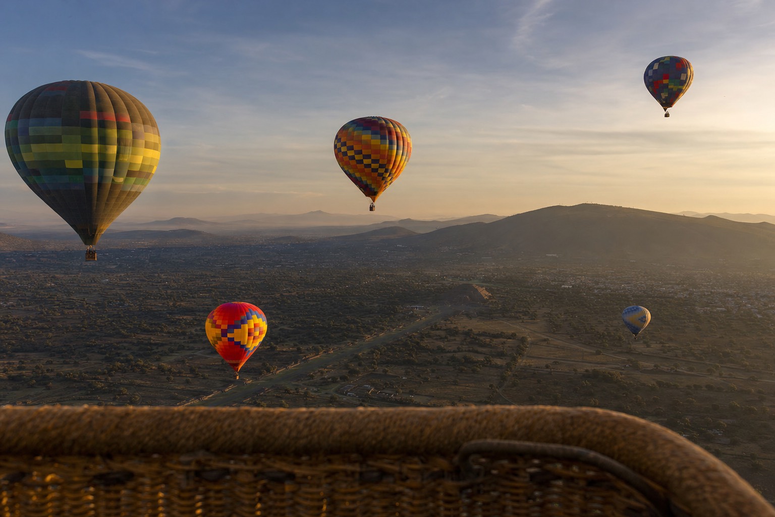 Other hot air balloons catching first light over the Teotihuacan valley, photographed from a balloon basket